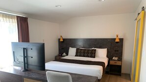 A hotel room with a bed, bedside table, desk, chair, TV, and a wardrobe. - Oasis Inn & Suites (Santa Barbara)