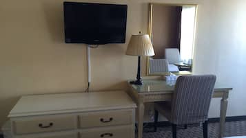 A hotel room with a flat-screen TV mounted on the wall, a lamp on a desk, a striped chair, and a dresser with drawers.