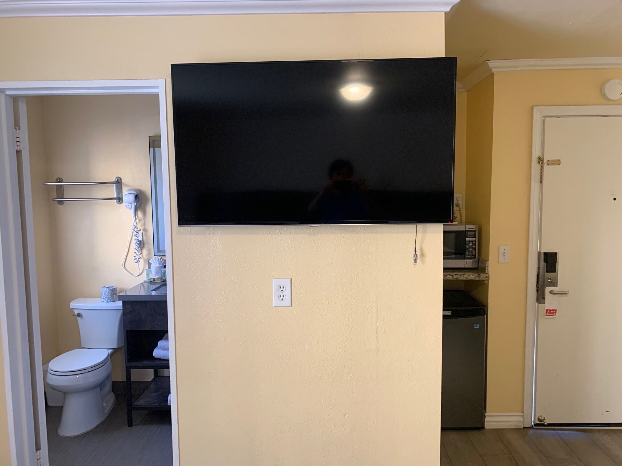 A bathroom with a toilet, a sink, and a mirror. There is a television mounted on the wall above the sink.