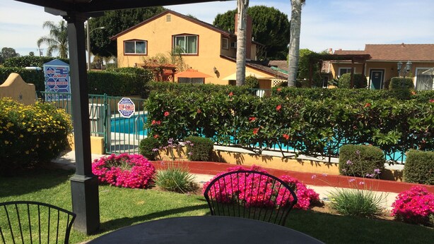 A patio area with a table and chairs, surrounded by vibrant flowers and a pool. - Oasis Inn & Suites (Santa Barbara)
