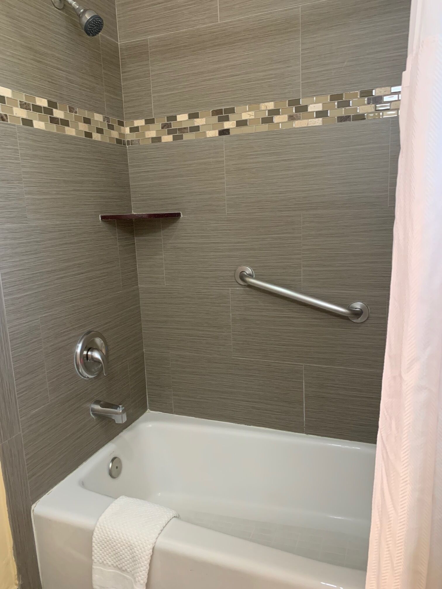 A bathroom with a bathtub, a showerhead, a grab bar, and a towel rack.