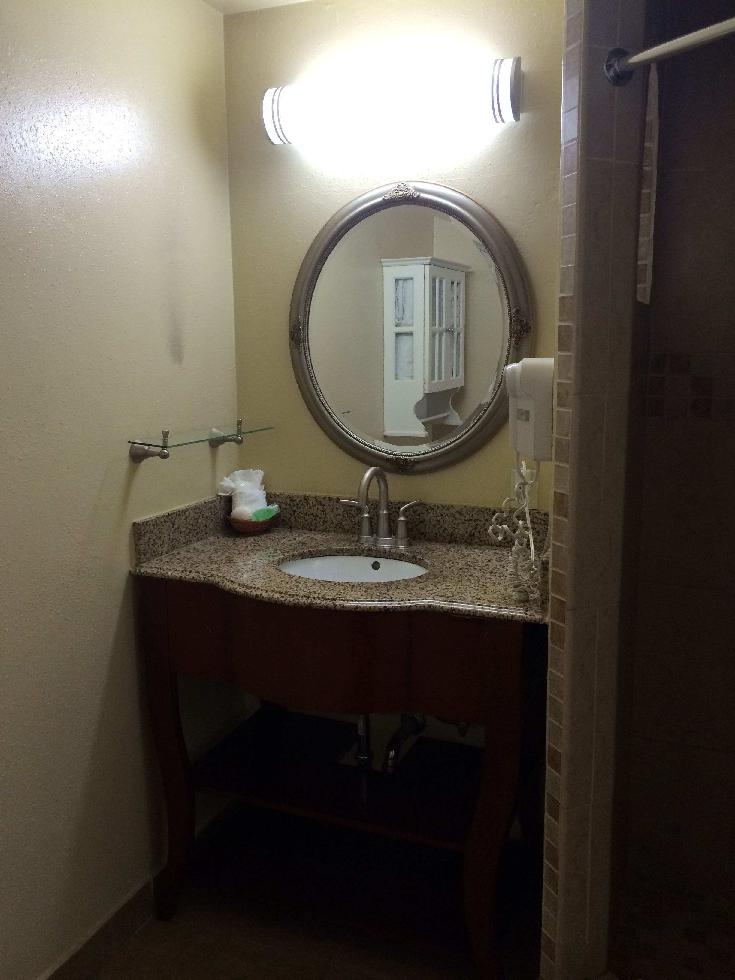 A bathroom with a granite countertop sink, a mirror, a towel rack, and a hand dryer.