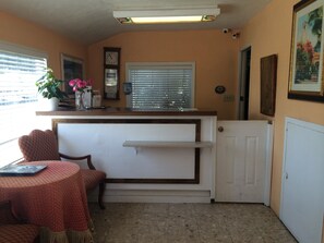 A compact kitchen with a white countertop, a window with blinds, a clock, and a door.
