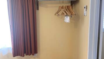 A room with a brown curtain, a bench, a wall-mounted air conditioner, and a wooden hanger rack with clothes.