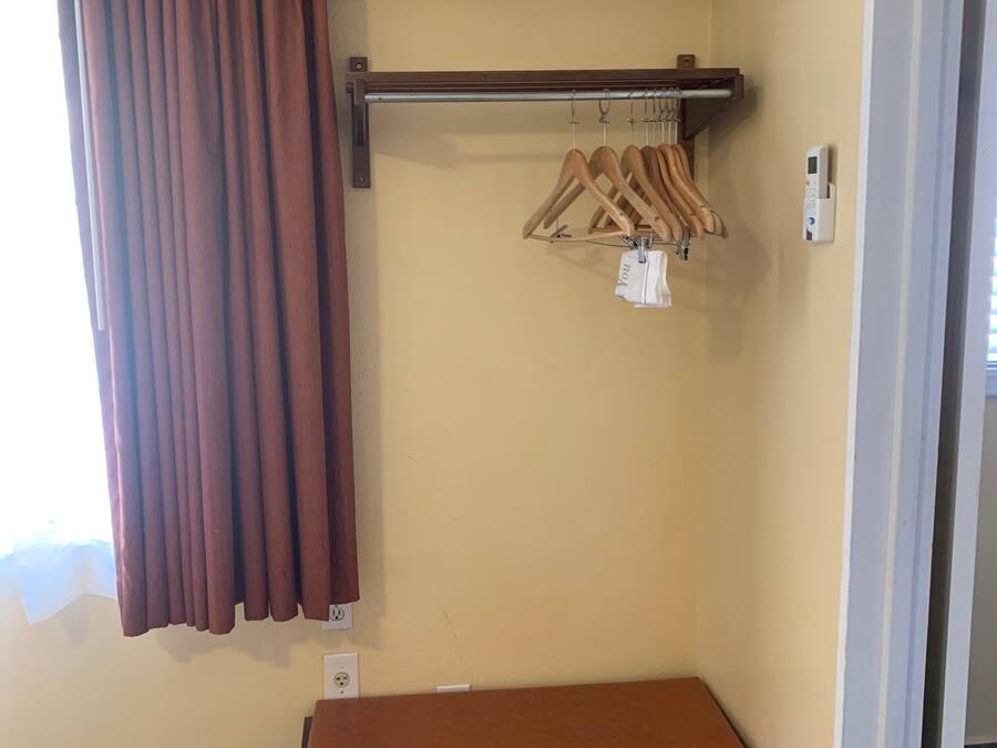 A room with a brown curtain, a bench, a wall-mounted air conditioner, and a wooden hanger rack with clothes.