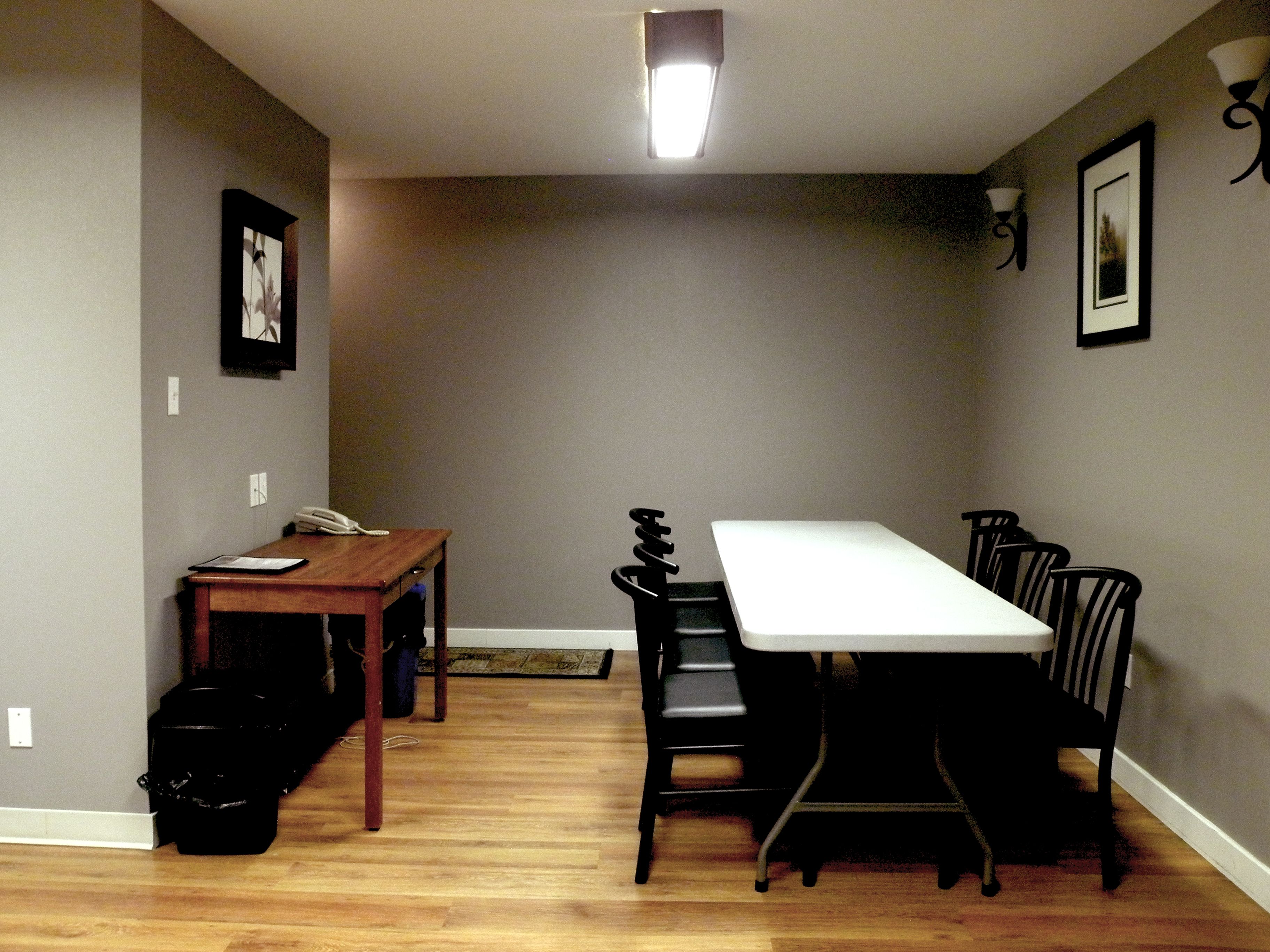 A dining area with a wooden table and chairs, a small table with a phone, and a black trash bin.