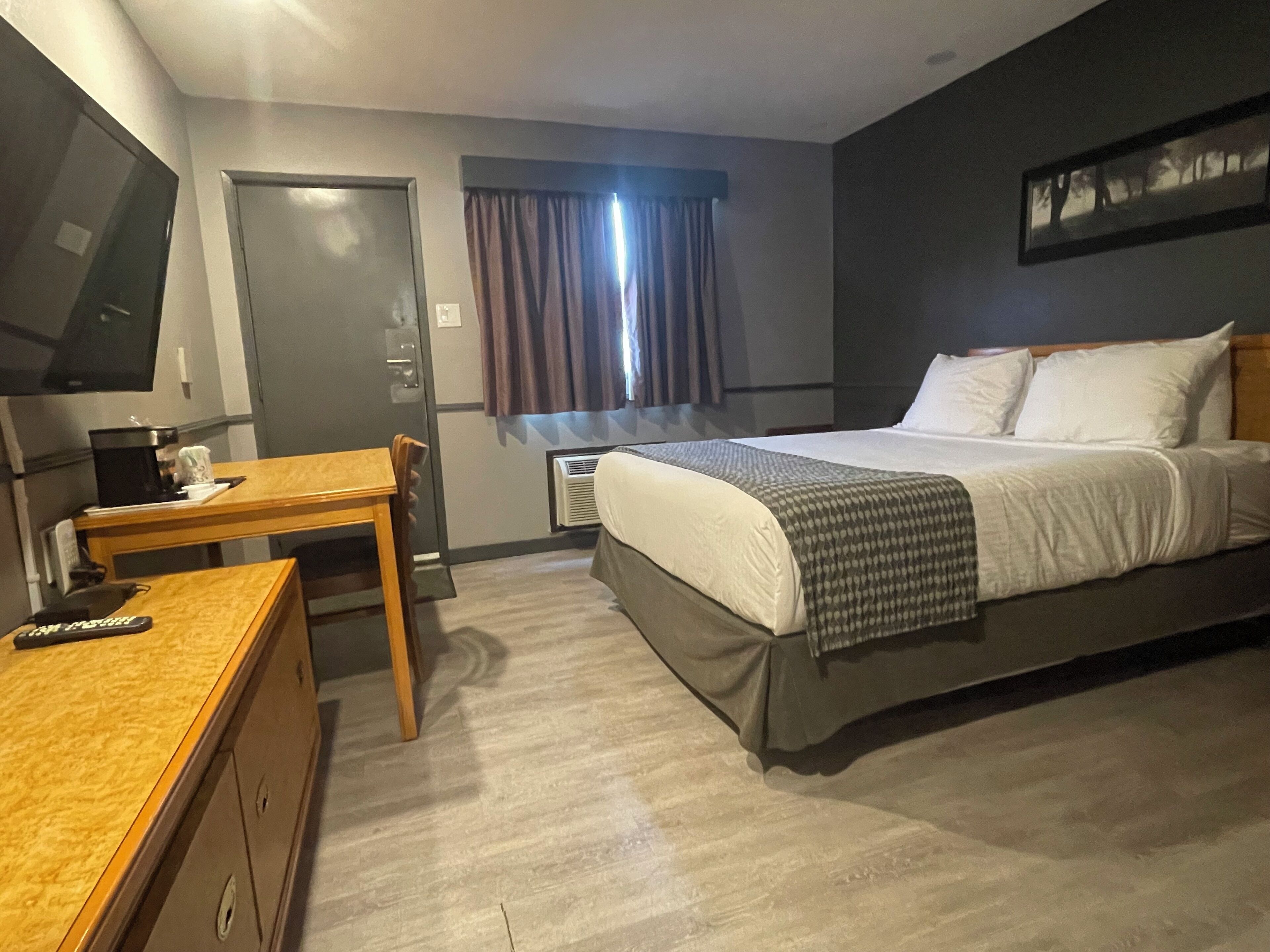 A hotel room with a bed, a desk, a chair, a TV, and a window with curtains.