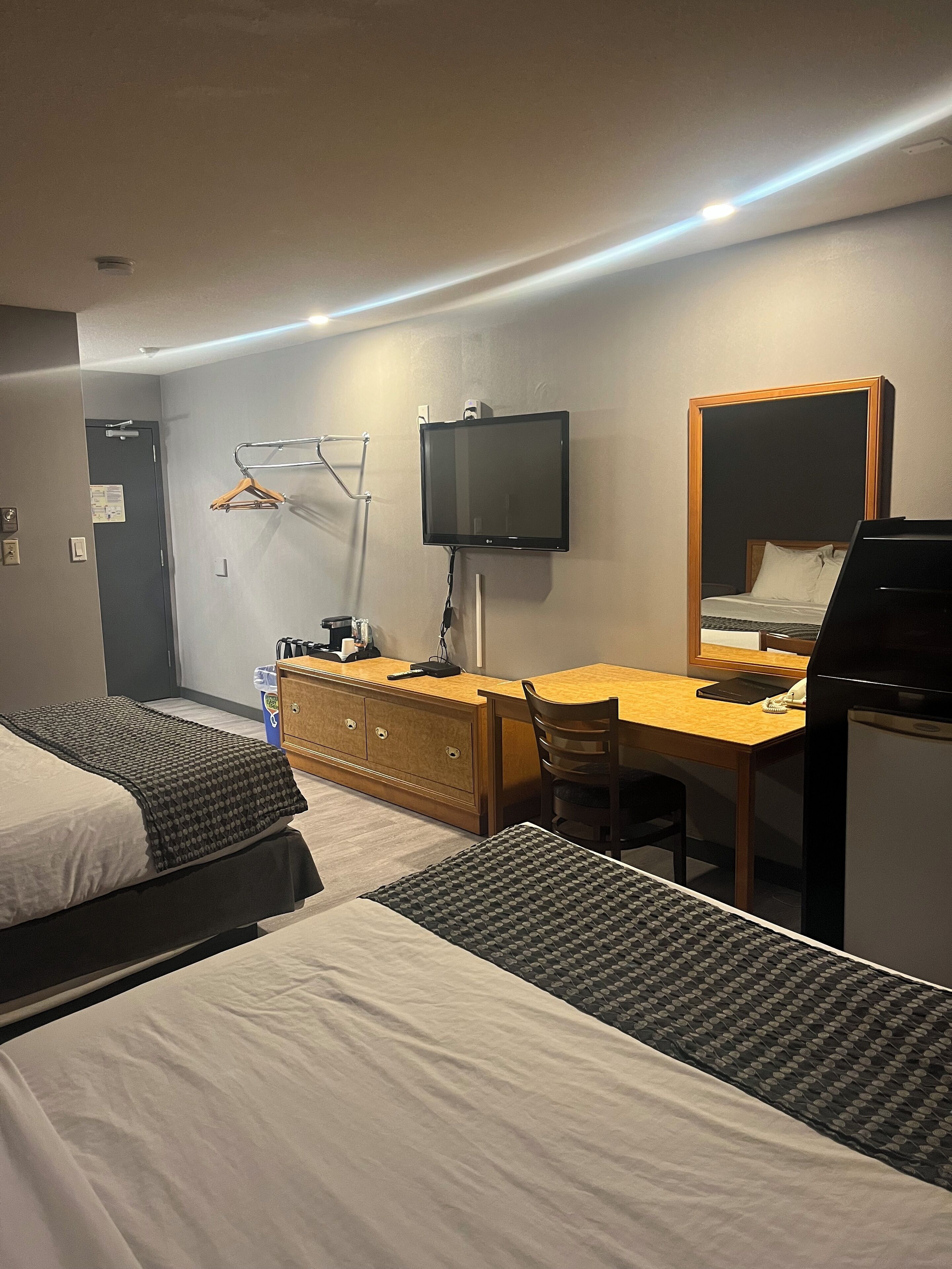 Une chambre d’hôtel avec deux lits, un bureau avec un ordinateur, une télévision et un réfrigérateur.
