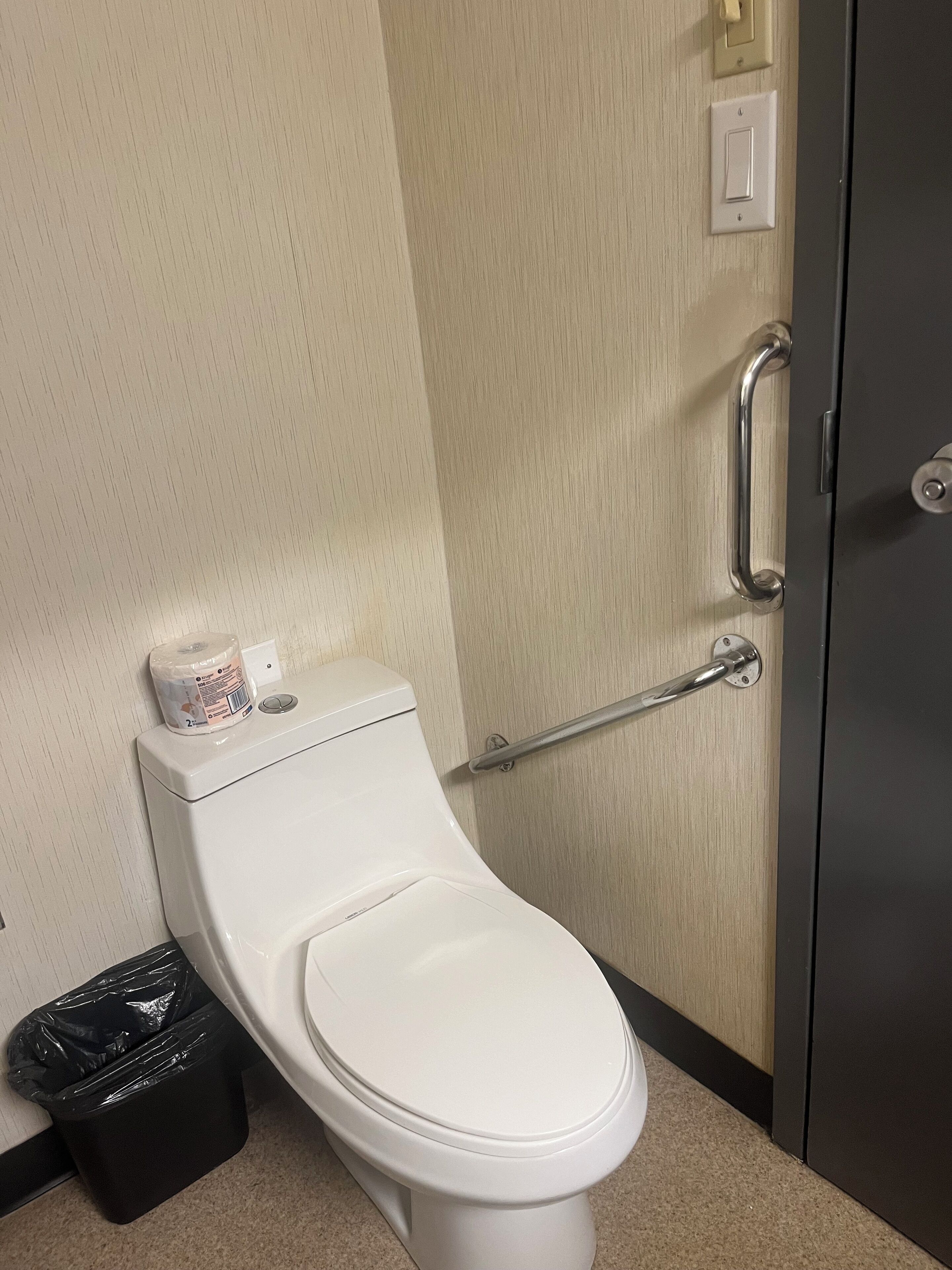 A white toilet with a trash can and a handrail in a bathroom.