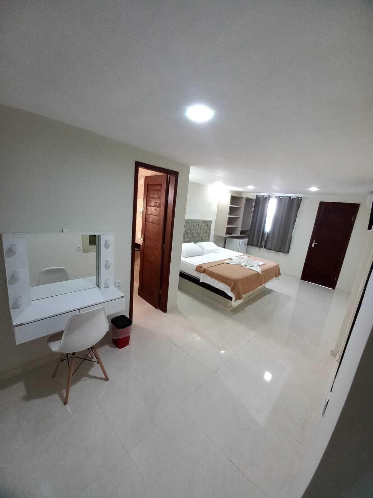 A bedroom with a bed, a vanity with a mirror, a chair, and a wardrobe.