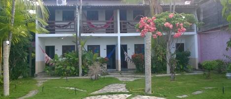 A two-story building with a garden in front, stone pathways, and a variety of plants.