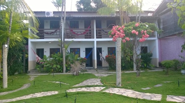 Un edificio de dos pisos con un jardín delantero, senderos de piedra y diversas plantas.