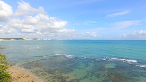 A beach with clear turquoise water, sandy shore, and distant hills. - Pousada Marajoara (Tibau do Sul)