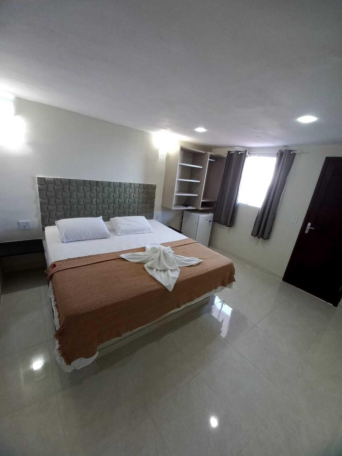 A hotel room with a large bed, a wardrobe, a small table, and a window with curtains.