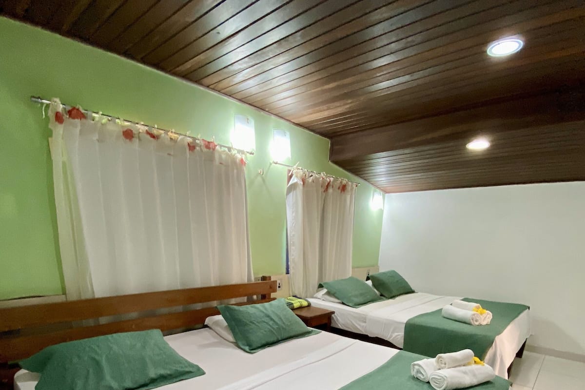 Ein Hotelzimmer mit zwei Betten, grüner Bettwäsche, weißen Vorhängen, einer Holzboden und einem gefliesten Boden.