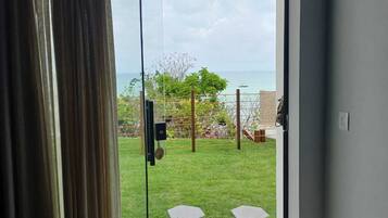 A room with a sliding glass door leading to a balcony with a view of the sea and a grassy area.