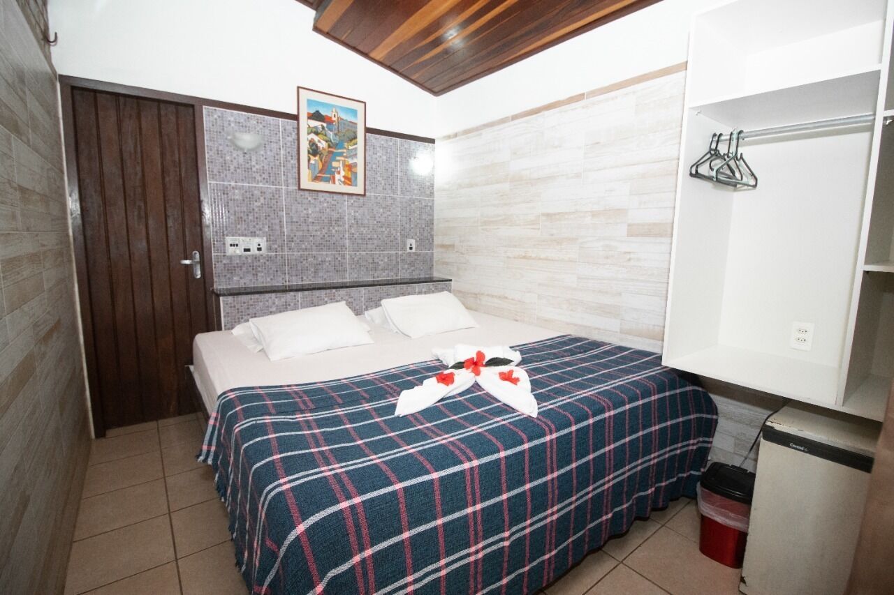 A bedroom with a bed, a wardrobe, a painting, and a small trash bin.