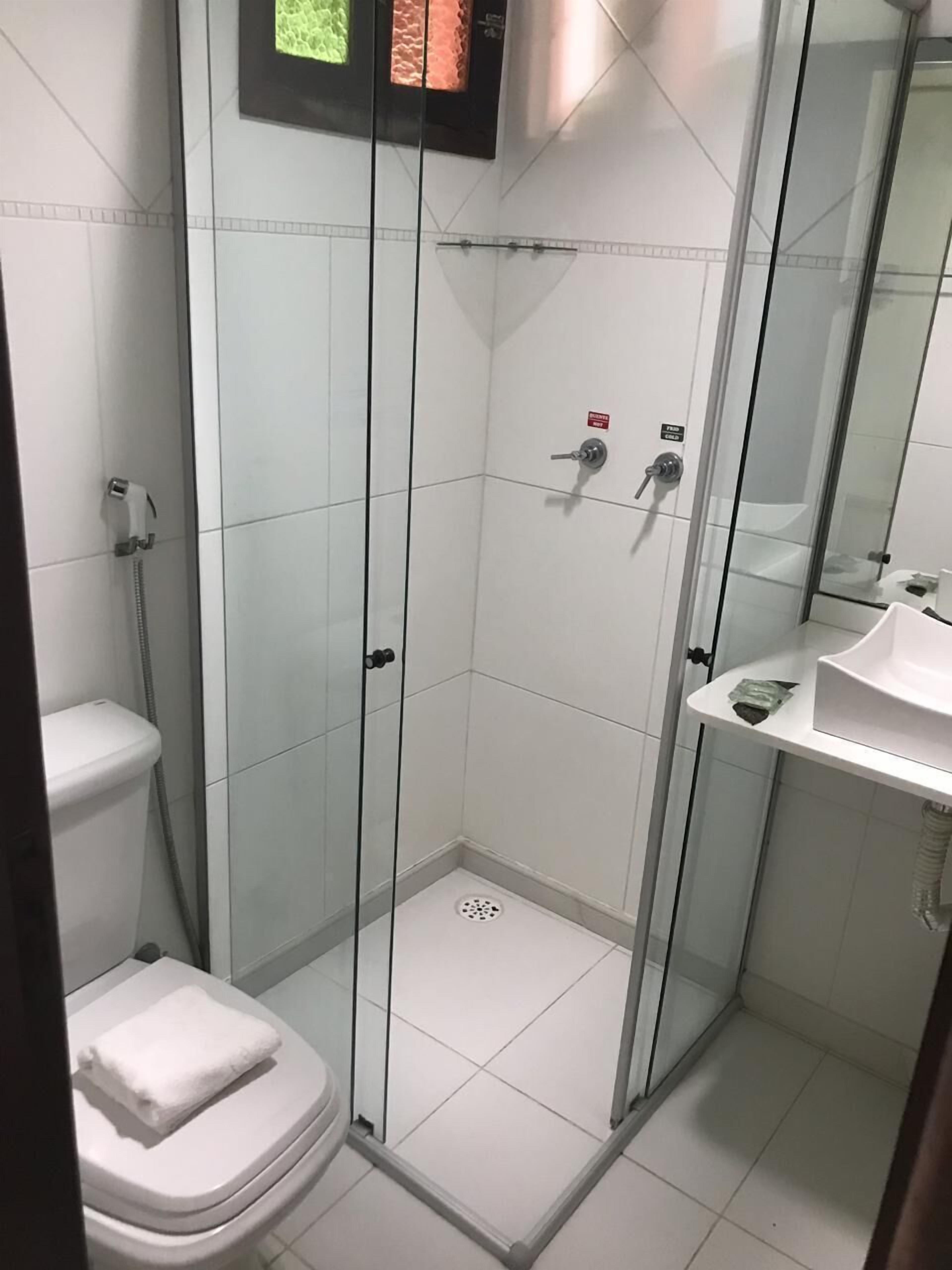 Egy modern fürőszoba üvegfalas zuhanyzóval, fehér WC-vel és tükörrel ellátott mosdókagylóval.