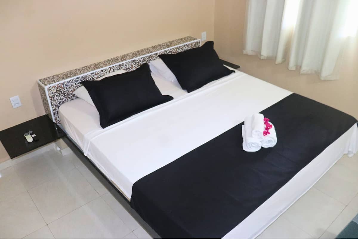 Ein Hotelzimmer mit einem großen Bett, schwarz-weißer Bettwäsche, einem schwarzen Kopfteil und einem kleinen Nachttisch mit Telefon und Fernbedienung.