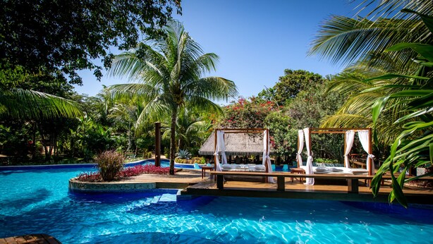 A pool area with a wooden deck, a thatched-roof structure, and a bed with white curtains. - Sombra e Agua Fresca Floresta (Tibau do Sul)
