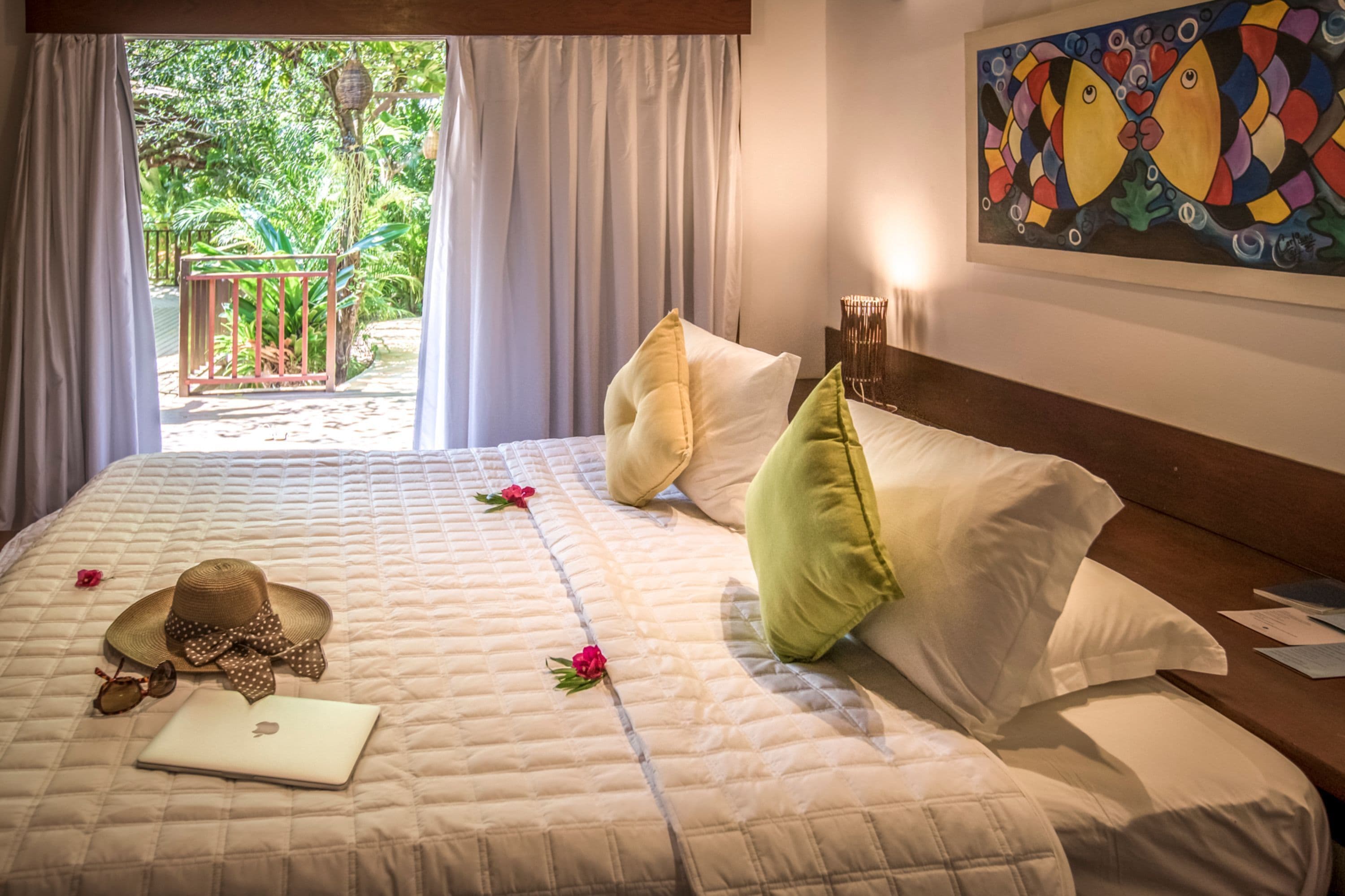 A bed with a laptop, a straw hat, and a flower on a quilted bedspread.