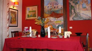 Un comedor con mantel rojo, un jarrón de flores y cuadros en la pared.