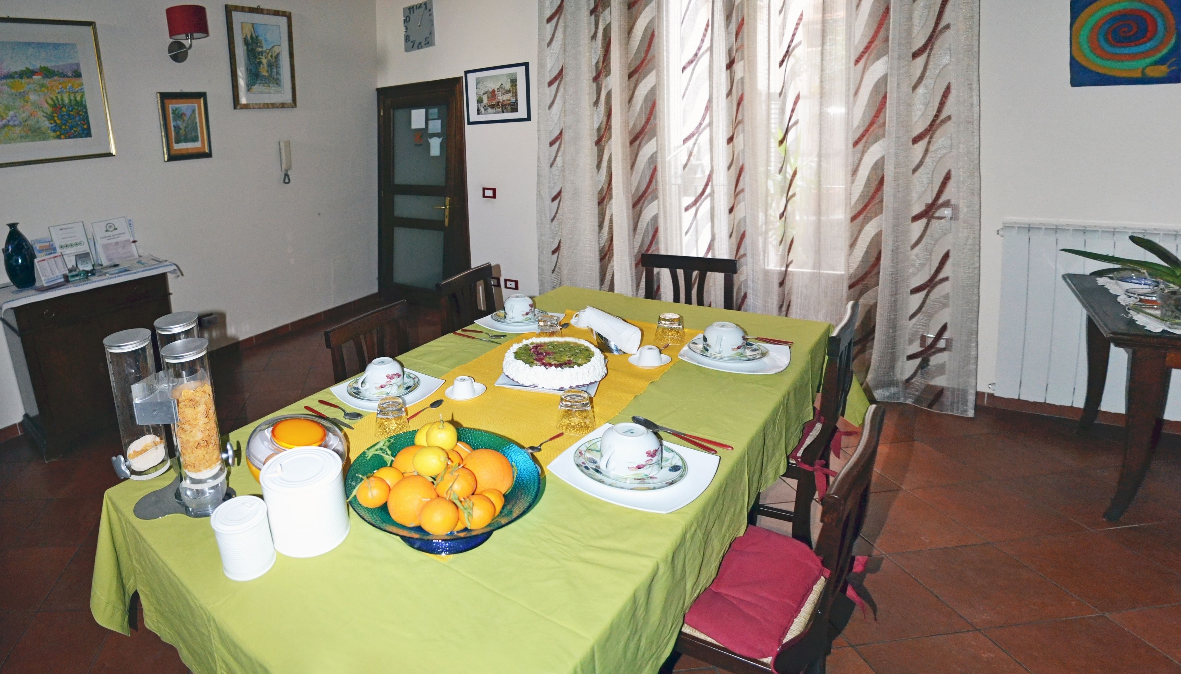 A dining room with a table set for a meal, featuring a cake, fruits, and various dishes.