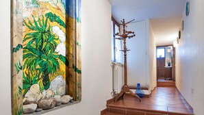 Un pasillo con piso de baldosas, una escalera y un cuadro grande con una escena tropical.