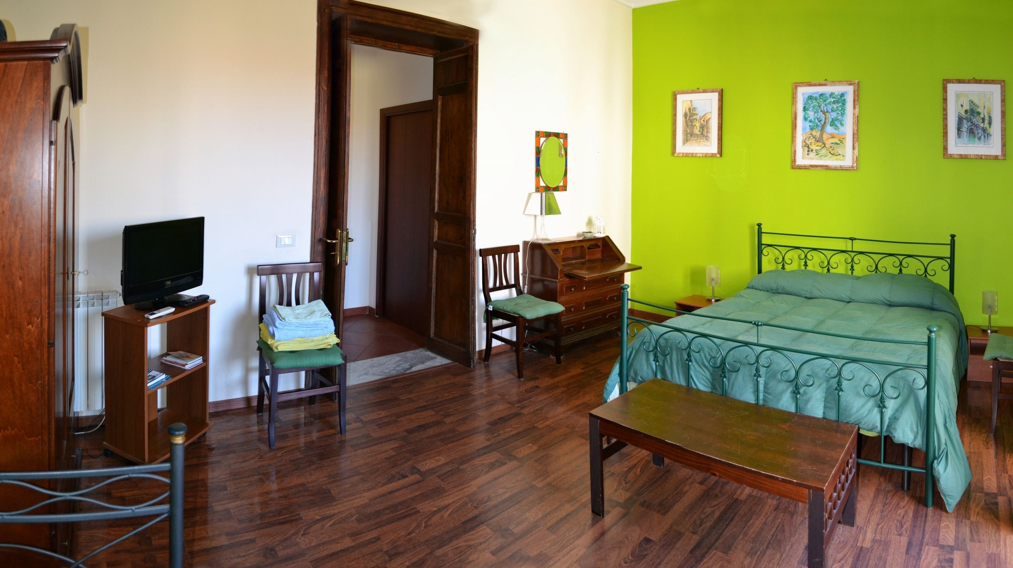 A room with a bed, a desk, a chair, a television, and a door.