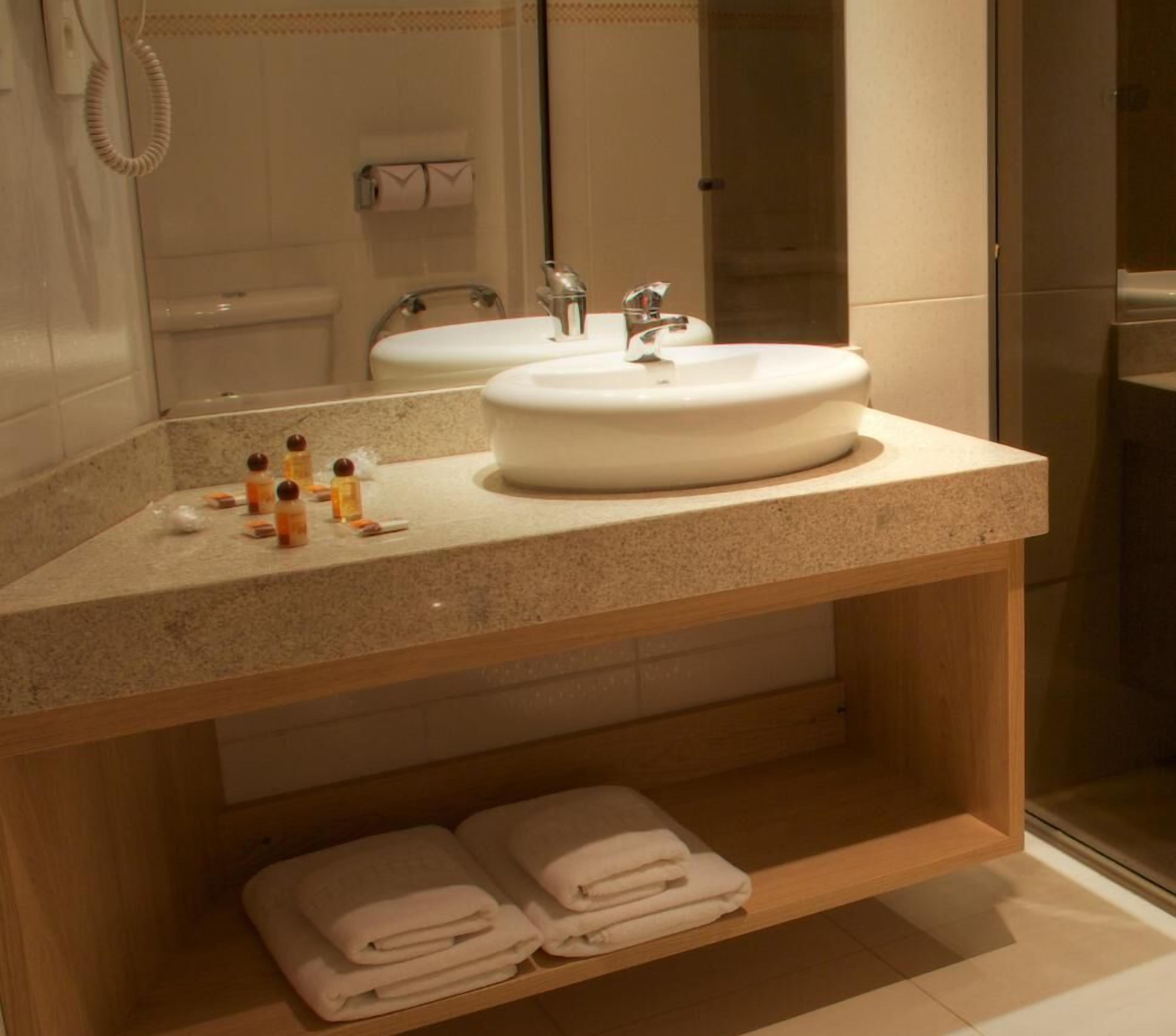 A bathroom with a large sink, a mirror, and a shelf with folded towels.