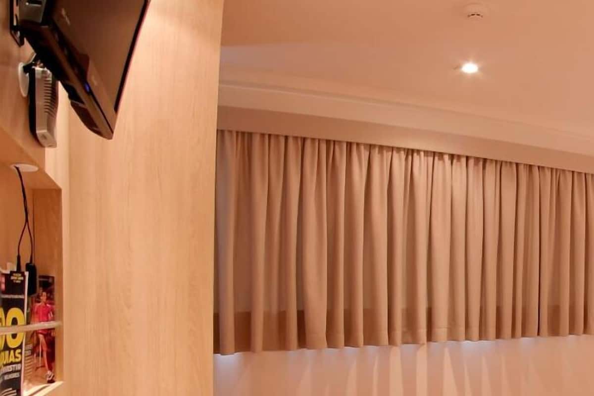Una habitación de hotel con cama, escritorio, silla, televisor y ventana con cortinas.
