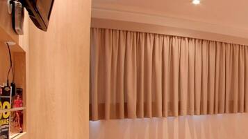 Una habitación de hotel con cama, escritorio, silla, televisor y ventana con cortinas.