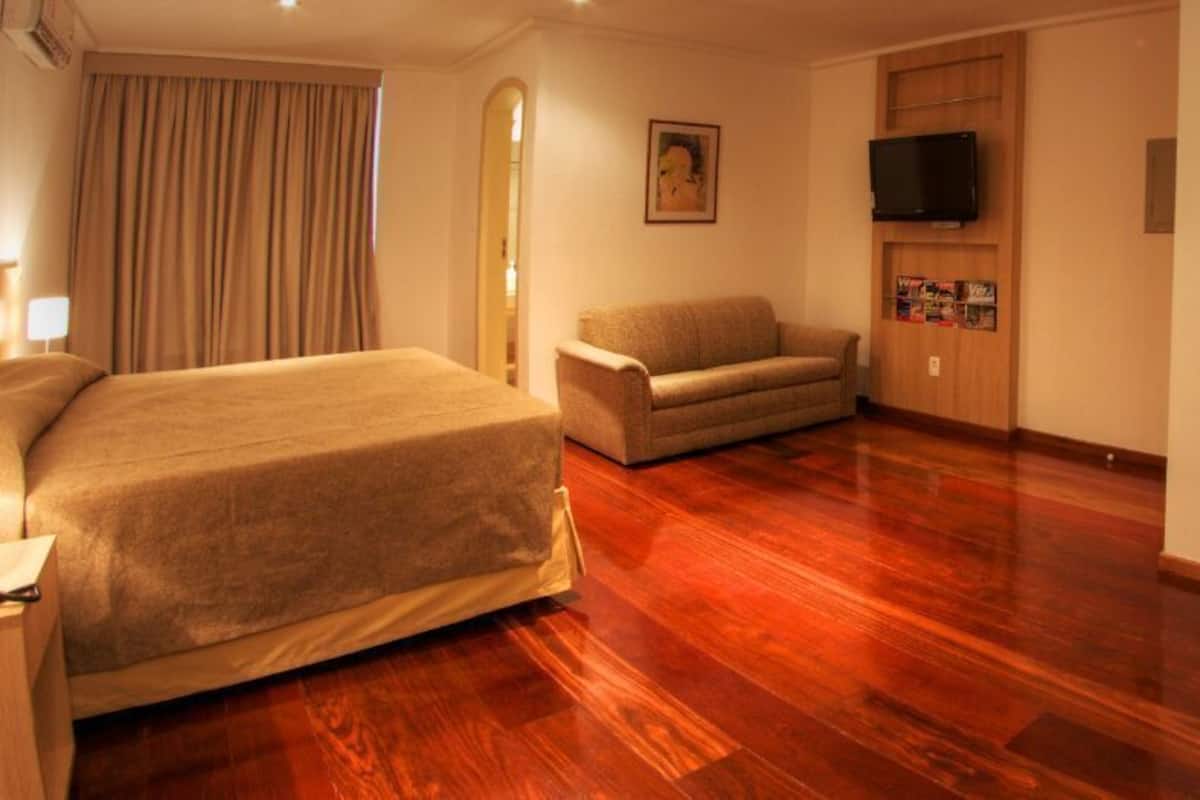 Habitación de hotel con cama, sofá, televisión en la pared y piso de madera.