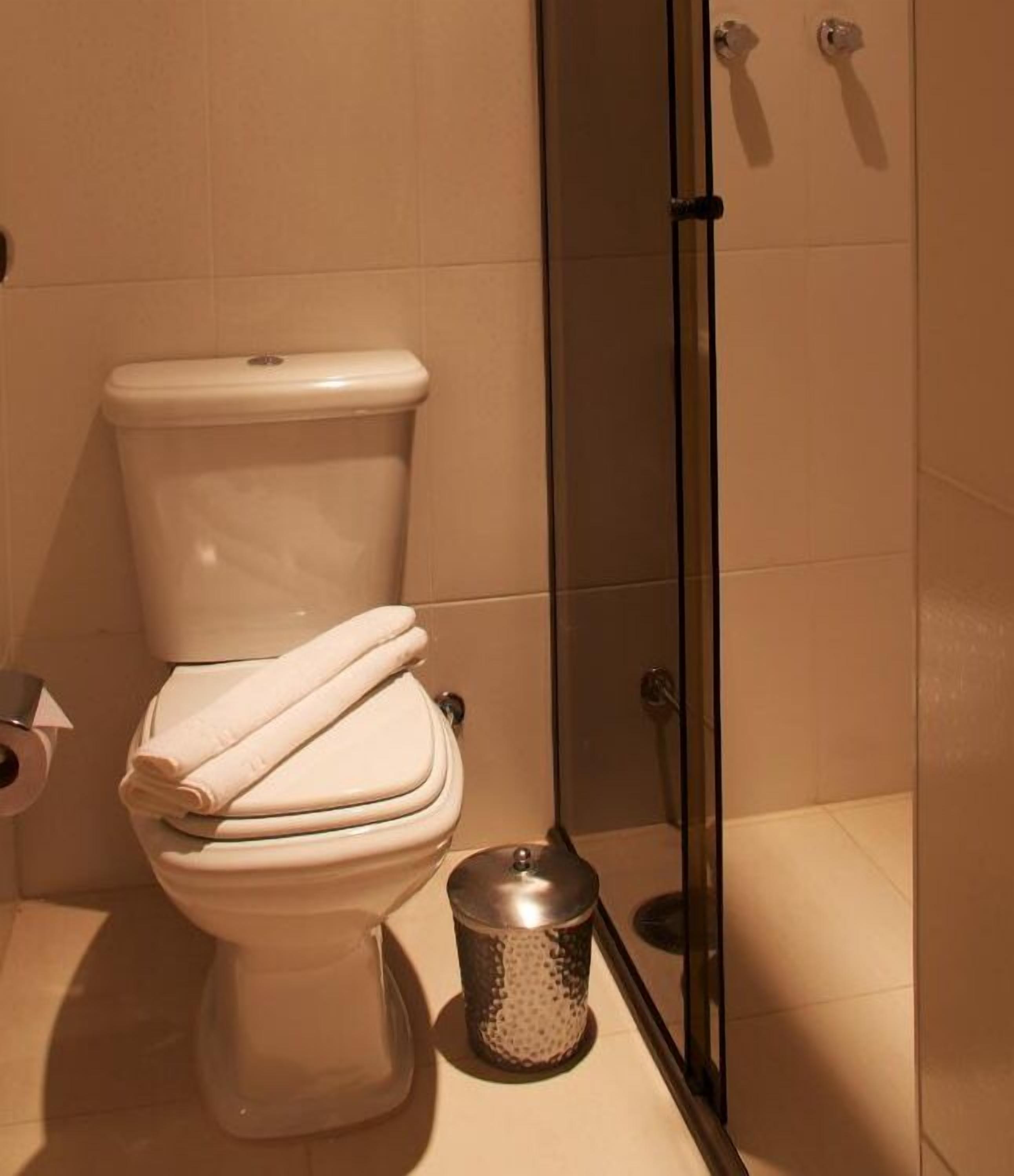 A bathroom with a toilet, a trash bin, and a shower area.
