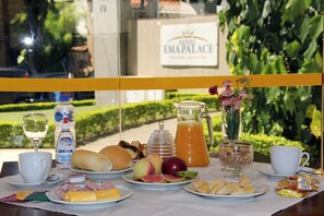 Una mesa de desayuno con diferentes alimentos, una botella de agua, un vaso de agua y un letrero del Hotel Emapalace al fondo.