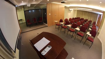 Una sala conferenze con un grande tavolo, sedie rosse, una lavagna e uno schermo per proiettore.