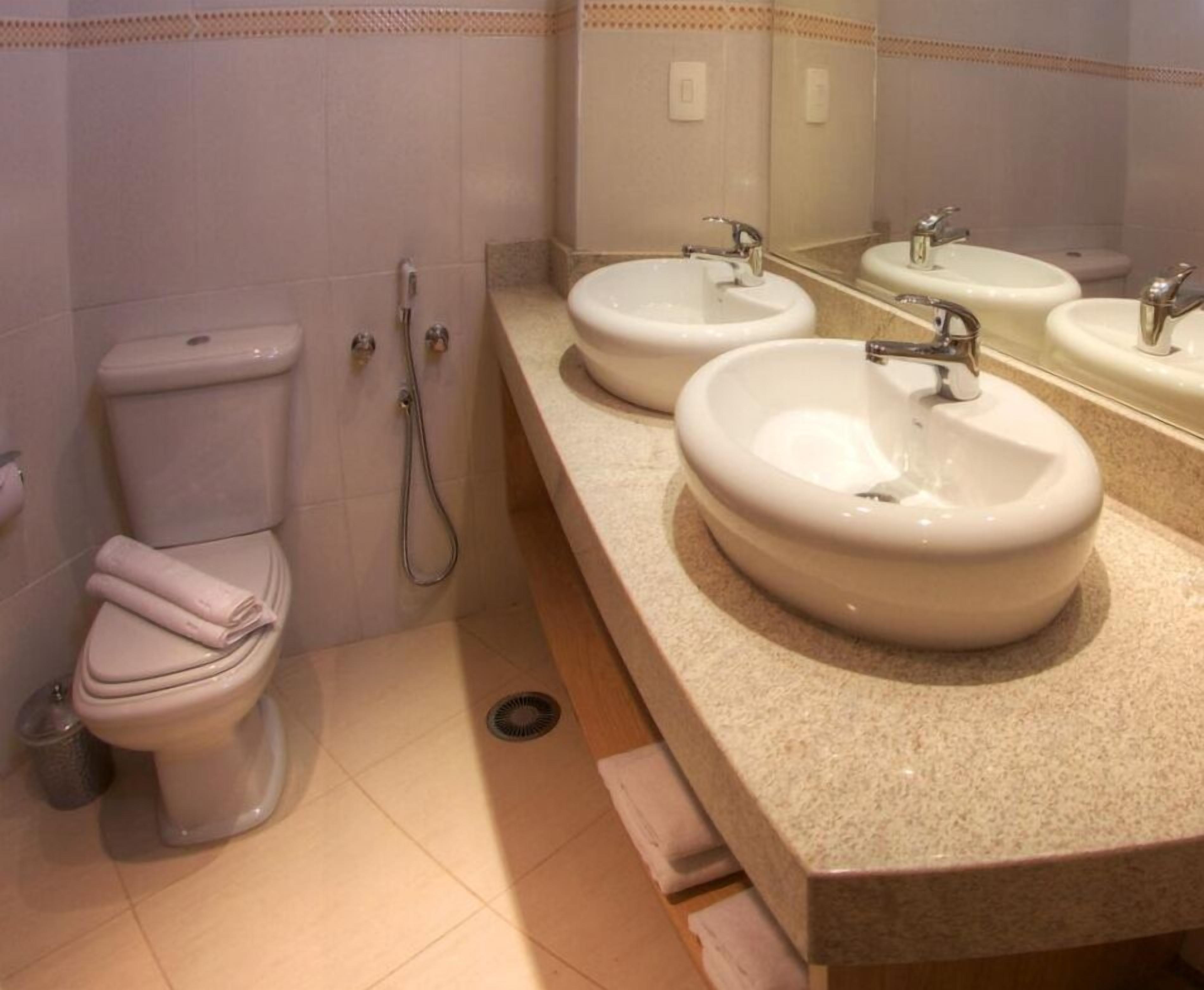 A bathroom with a toilet, two sinks, and a shower.