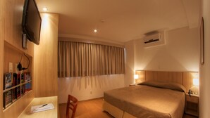 Hotelkamer met een bed, bureau, stoel, tv aan de muur en raam met gordijnen.