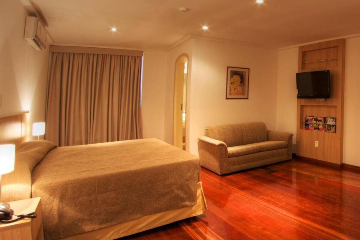 Una habitación de hotel con una cama grande, un sofá, un televisor y un armario de madera.