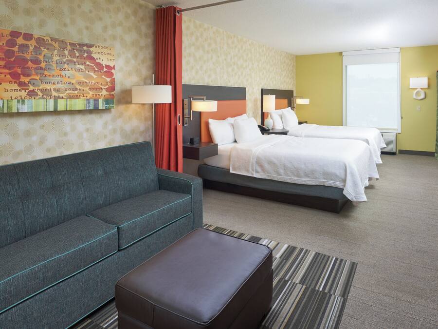 Ein Hotelzimmer mit einer Couch, zwei Betten, einem Schreibtisch und einem Gemälde an der Wand.