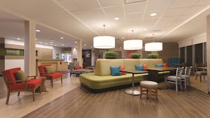 A modern hotel lobby with a green sofa, red chairs, a wooden table, and pendant lighting.