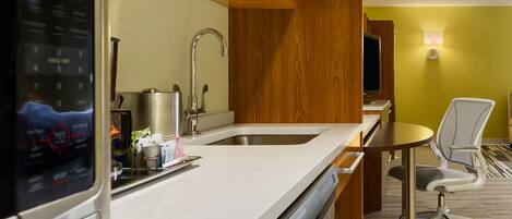 A modern kitchen with a built-in dishwasher, a stainless steel sink, and a small dining area with a chair.