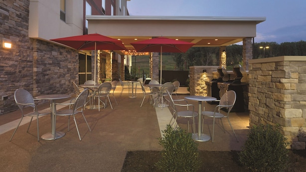 An outdoor patio area with stone walls, metal tables, and chairs, featuring string lights and a barbecue grill.