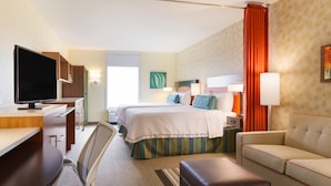 A hotel room with a desk, two beds, a TV, and a sofa.