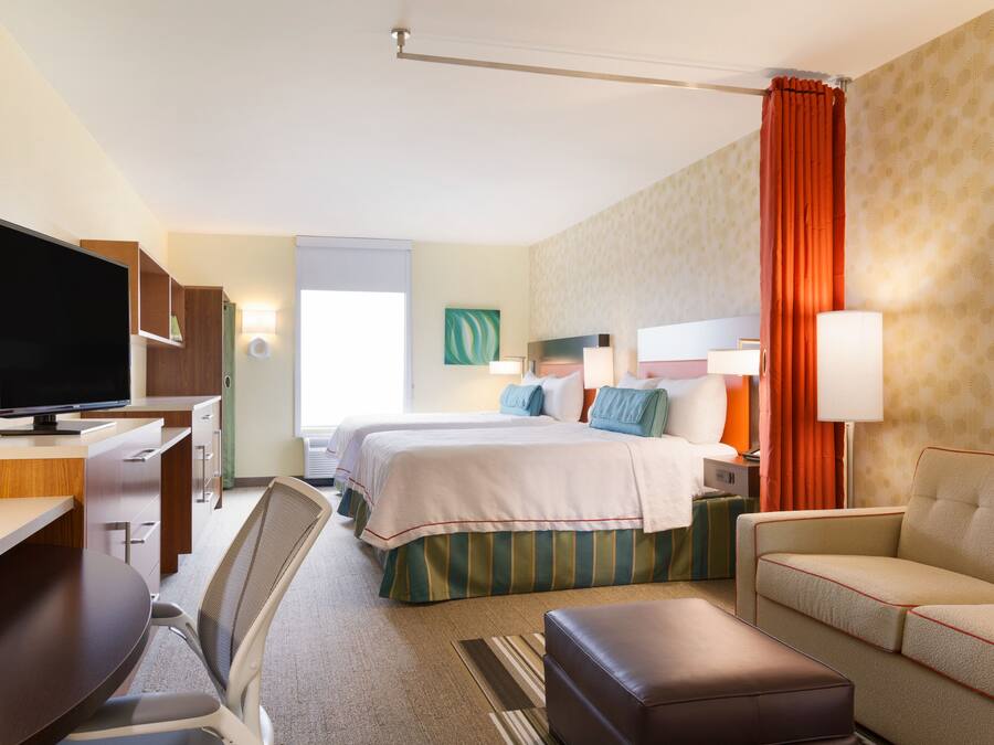 Ett hotellrum med ett skrivbord, två sängar, en TV och en soffa.
