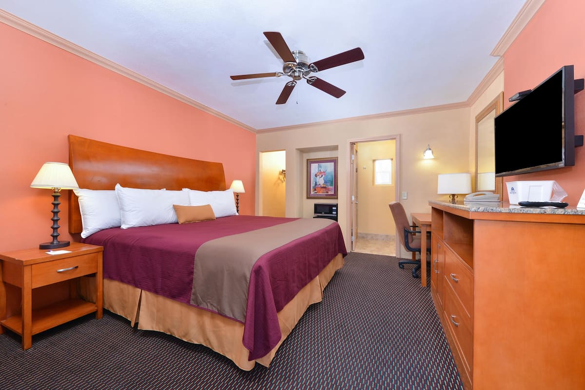 A hotel room with a bed, a desk, a television, and a ceiling fan.