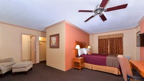 A hotel room with a bed, a desk, a chair, a ceiling fan, and a door.