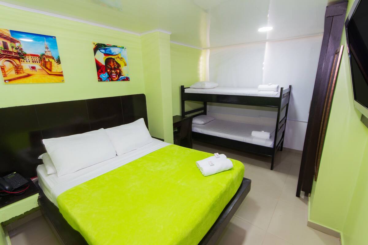 A hotel room with a bed, bunk beds, a telephone, and artwork on the wall.