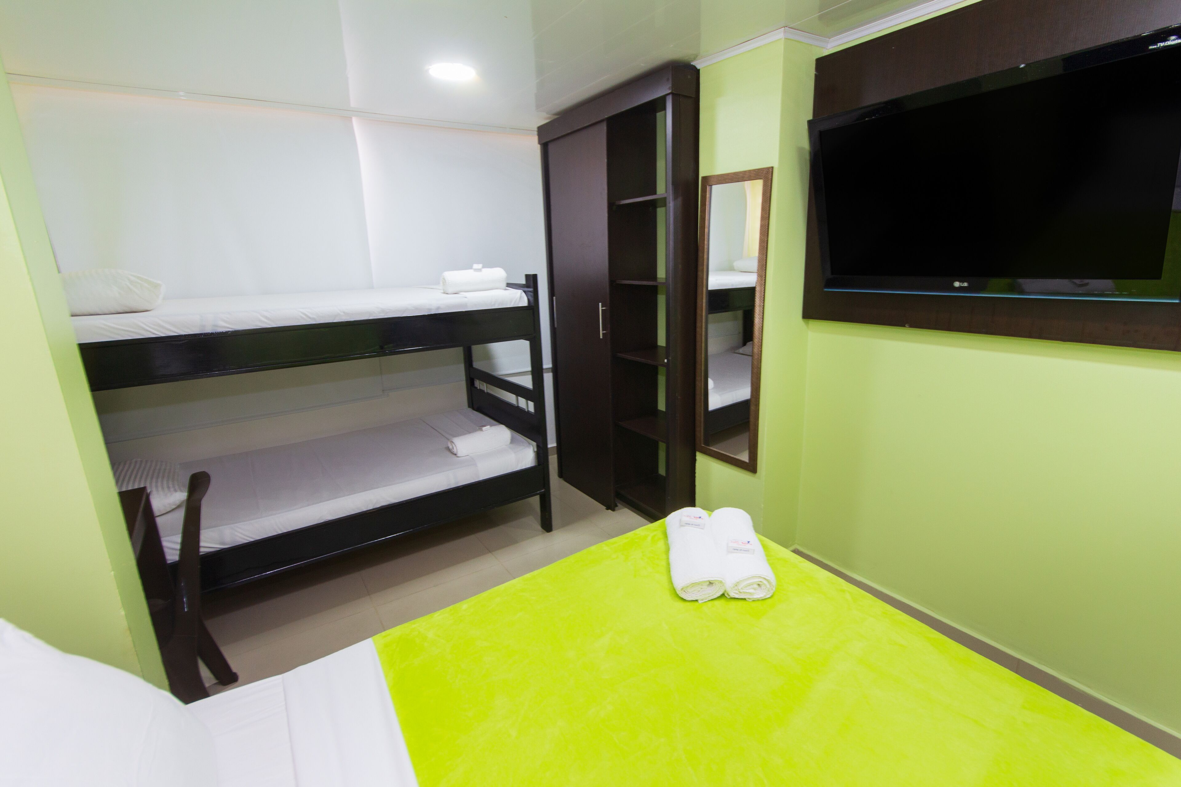A room with bunk beds, a wardrobe, a flat-screen TV, and a green mat.