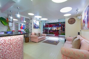 A reception area with a tiled mosaic wall, a reception desk, two patterned sofas, and a large painting on the wall. - Hotel Marina Suites By Geh Suites (Cartagena)